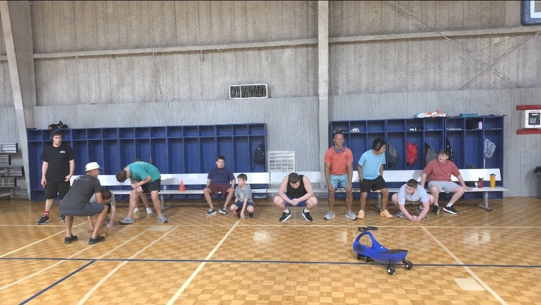 The group gathers on benches along the gym wall between activities.