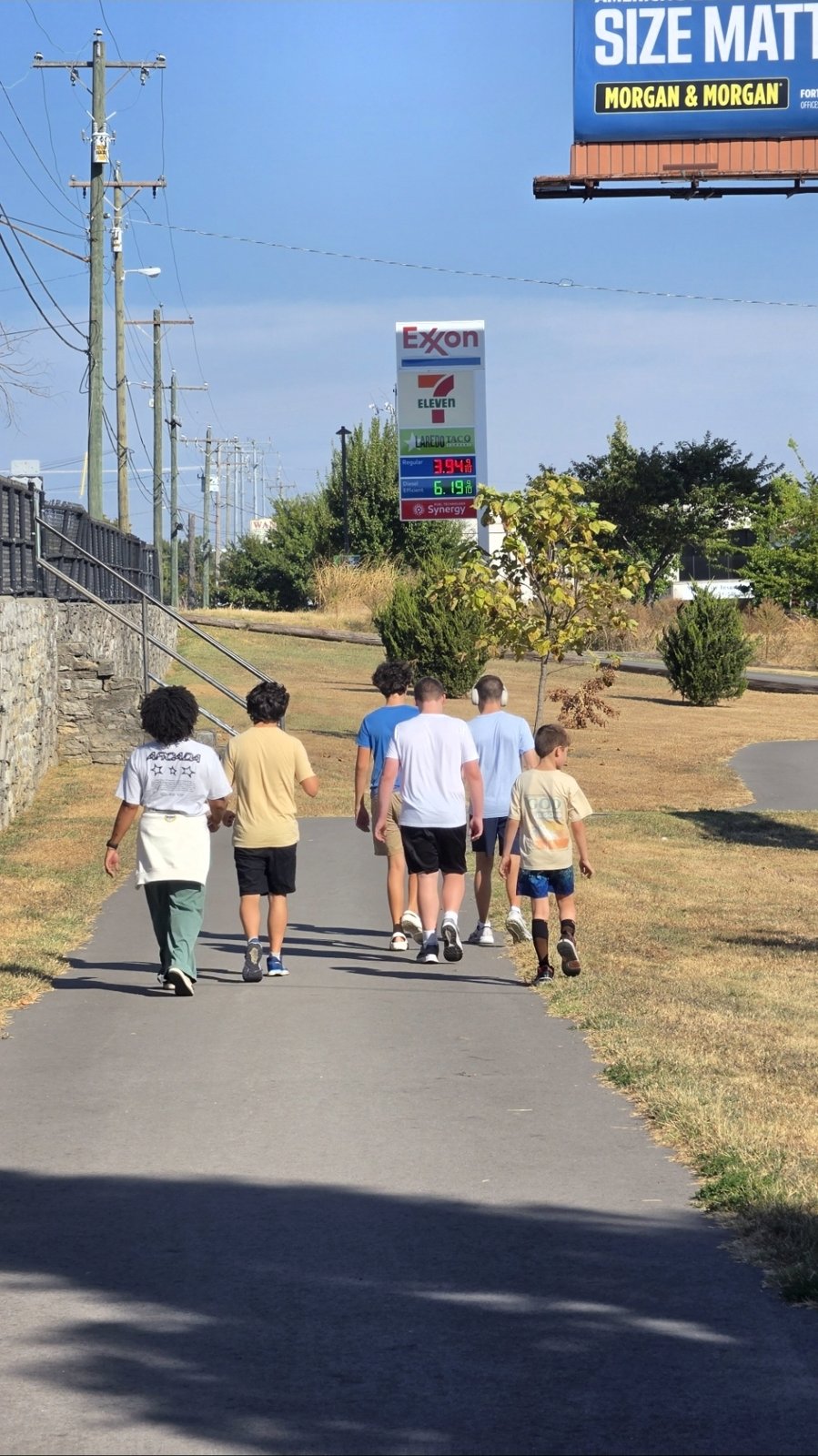 The group walks together along a paved trail on a sunny day.