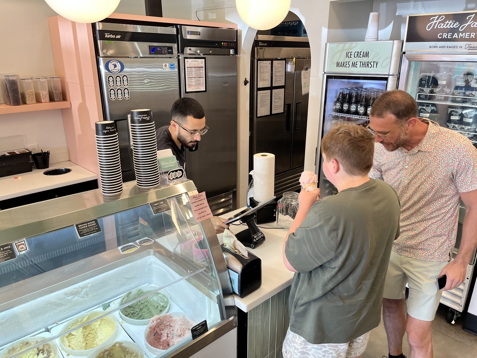 A young person orders at an ice cream shop counter with support from an adult.