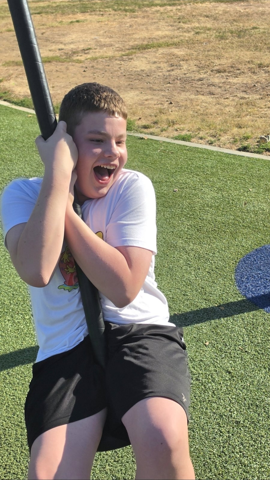 A laughing boy rides a playground zip-line on a sunny day.