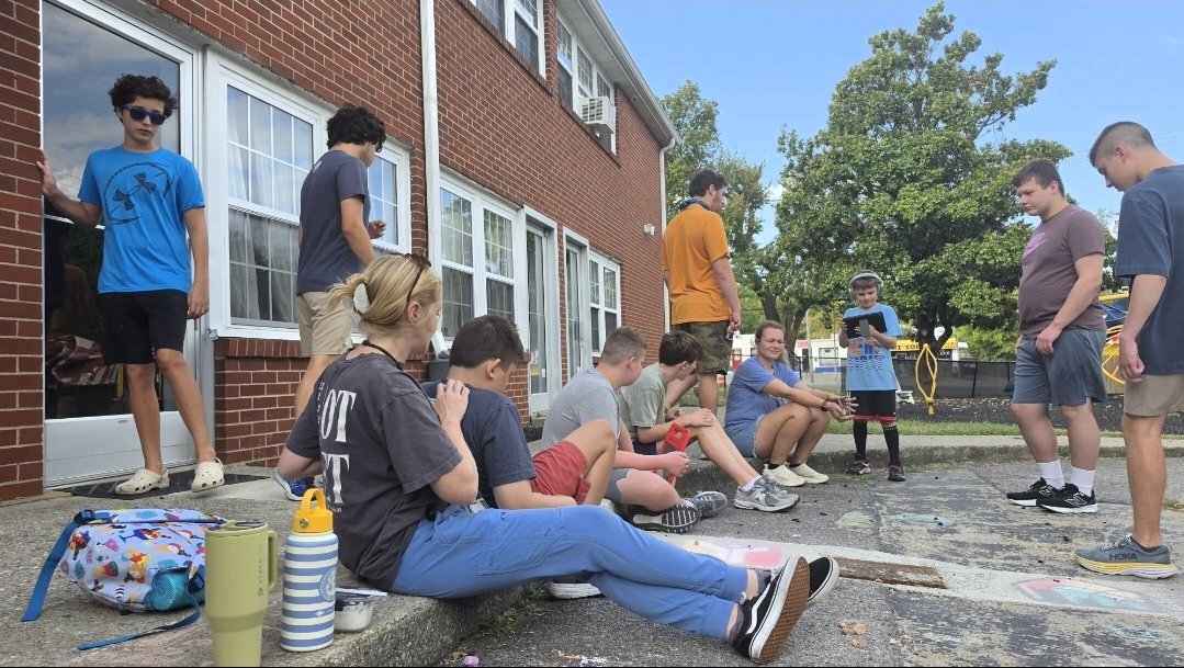 The group relaxes together on the pavement outside the building.