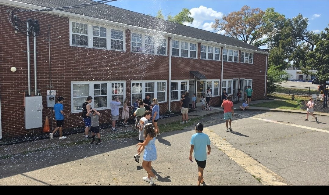 Kids splash through a spray of water outside the building on a sunny day.