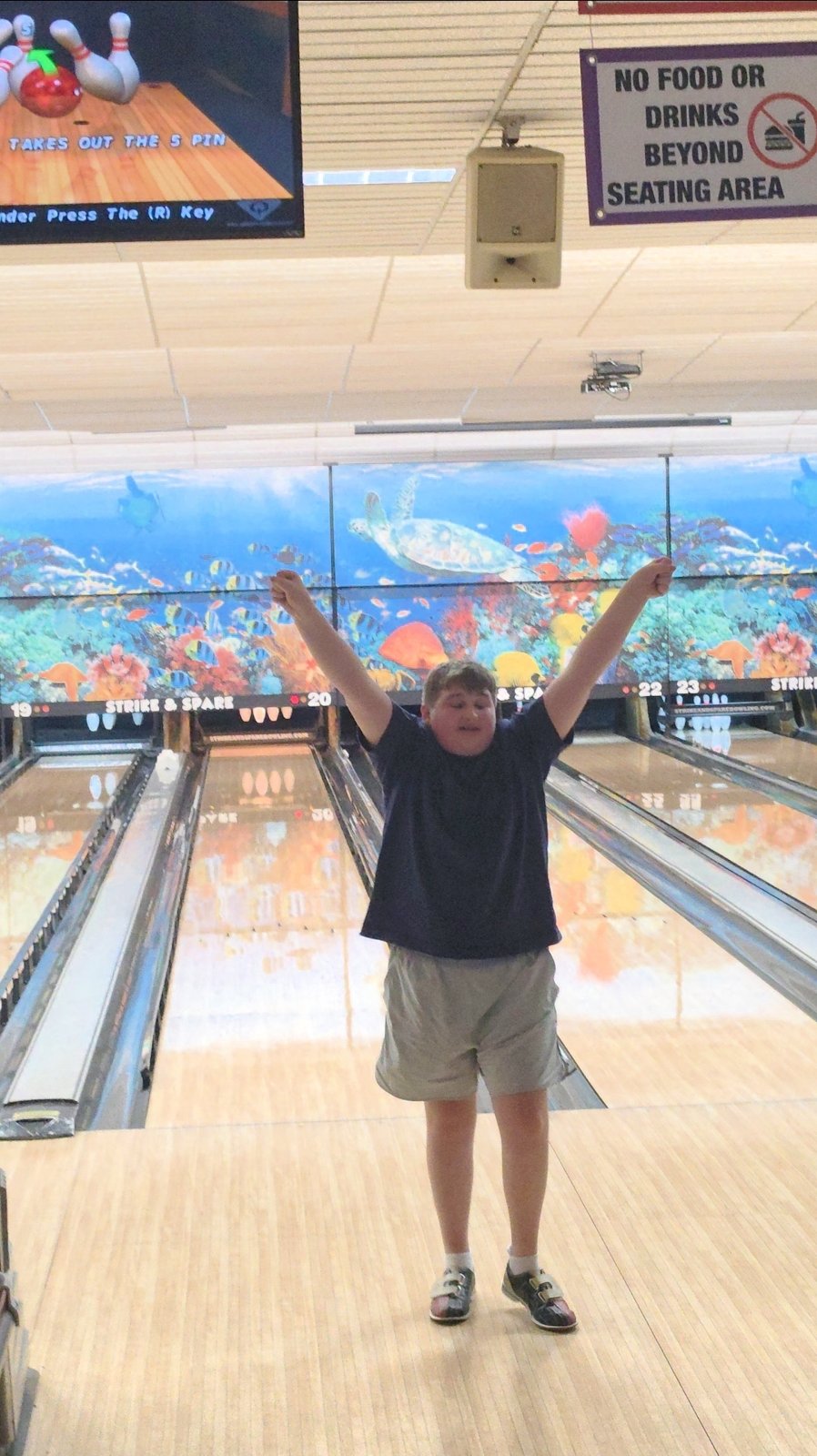 A boy raises both arms in celebration at the bowling lanes.