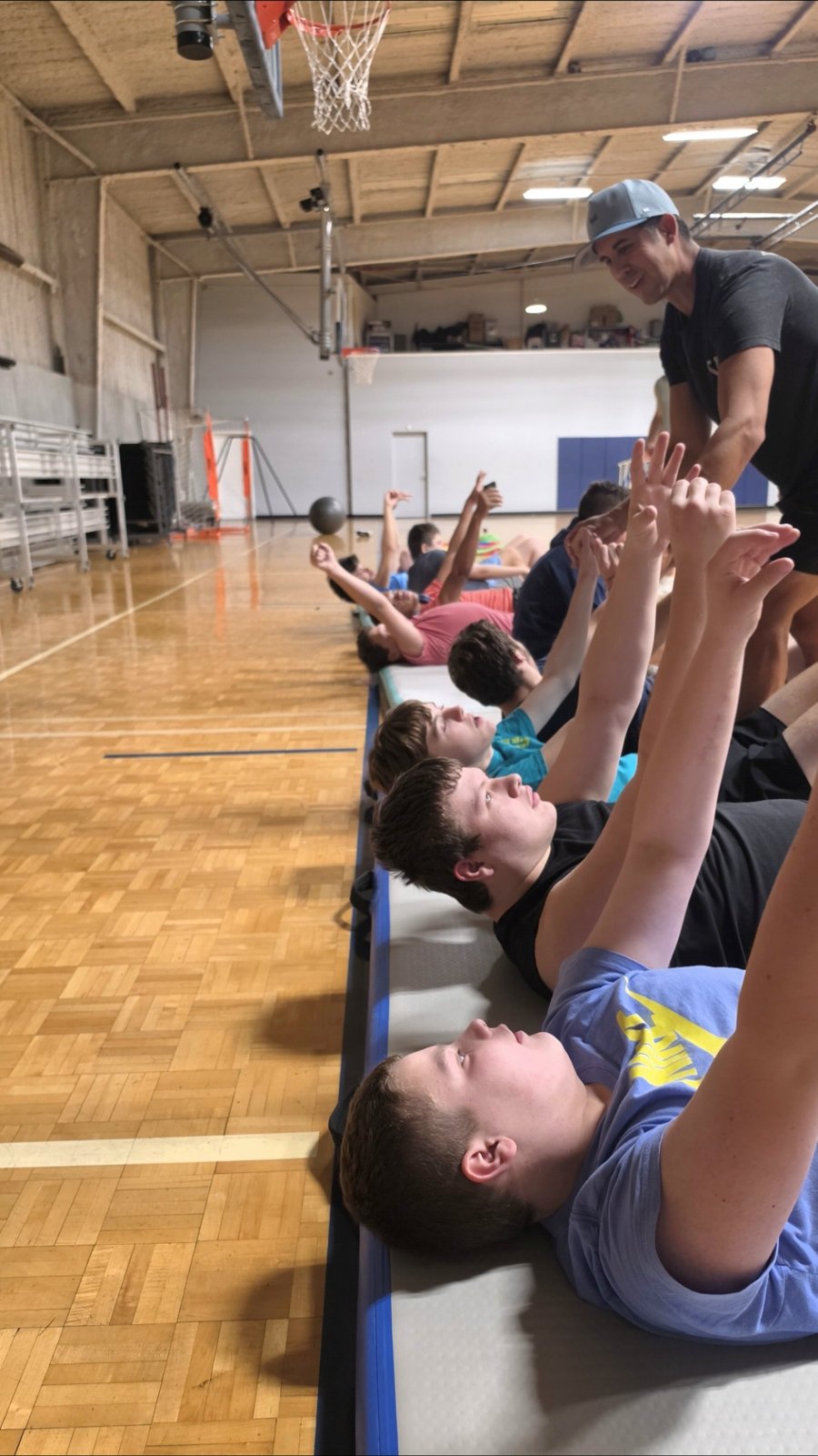 A coach leads a group of kids through a floor exercise in the gym.