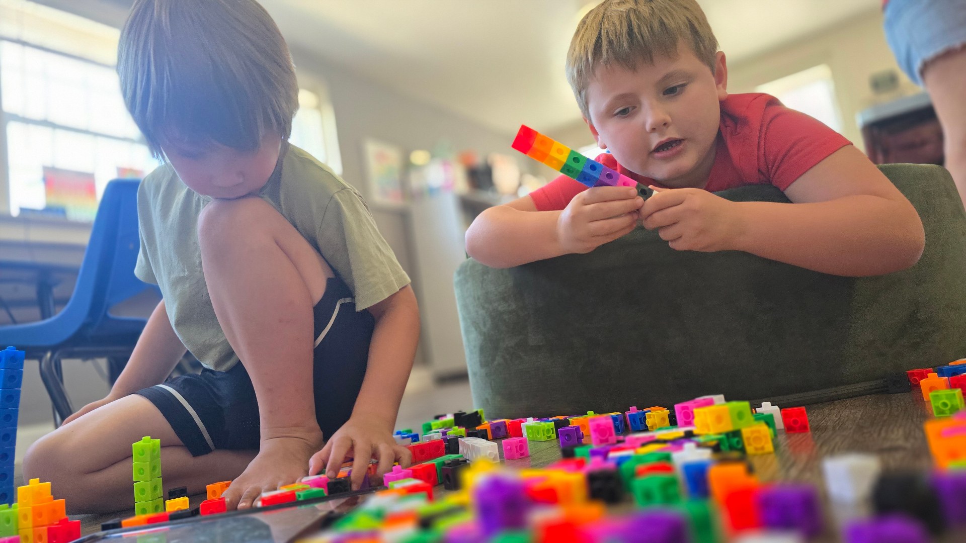 Two children sit on the floor building with colorful blocks.